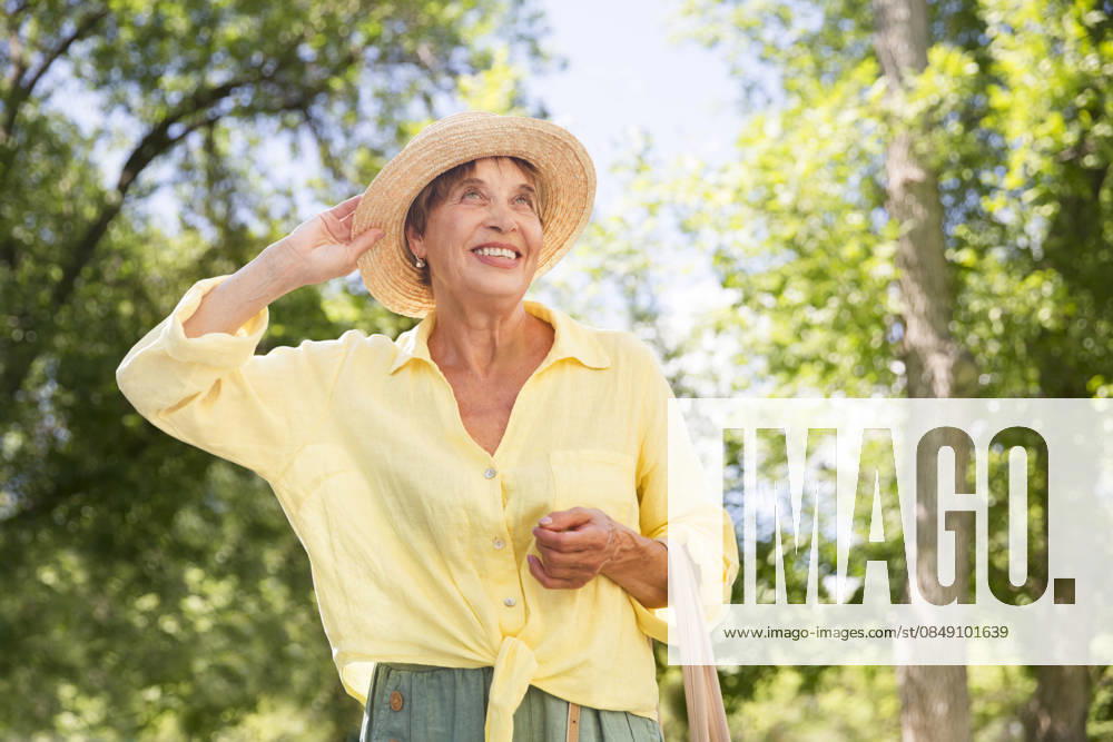 Glückliche ältere Frau mit Sonnenhut spaziert durch die Sommerstadt happy senior woman in sun hat walks on summer city (License=RF) ,model released, Symbolfoto