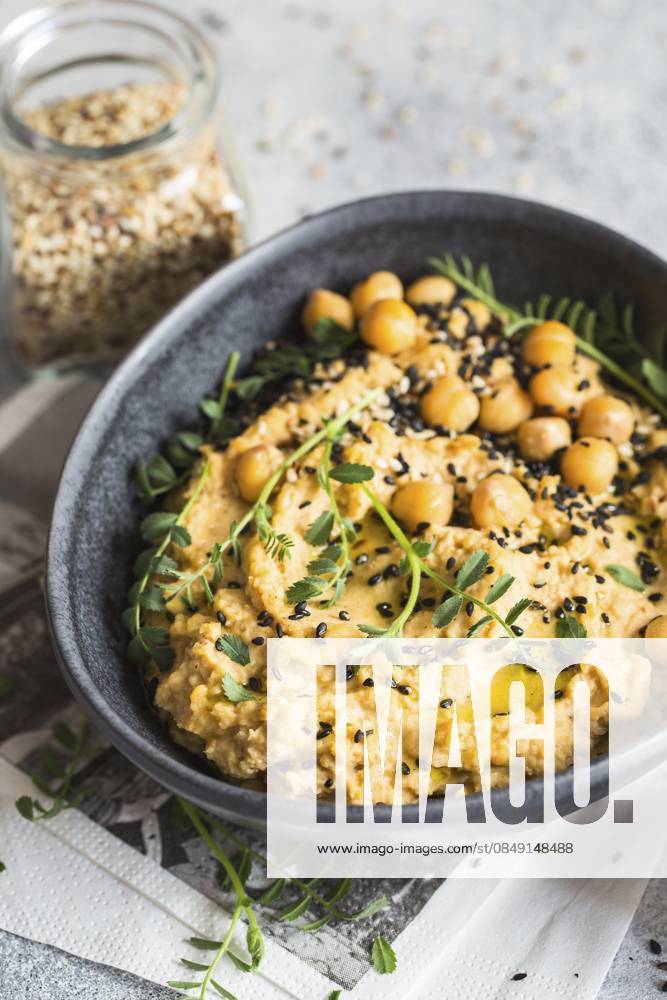Kichererbsenhummus in der schwarzen Schale, dekoriert mit Sesamsamen und Kichererbsengrün. Vegane Rezepte, Gerichte auf pflanzlicher Basis. Konzept für umweltfreundliches Wohnen. Biologische Lebensmittel. Vegetarische Küche Chickpeas hummus in the black bowl decorated with sesame seeds and chickpeas greens. Vegan recipes, plant-based dishes. Green living concept. Organic food. Vegetarian cuisine
