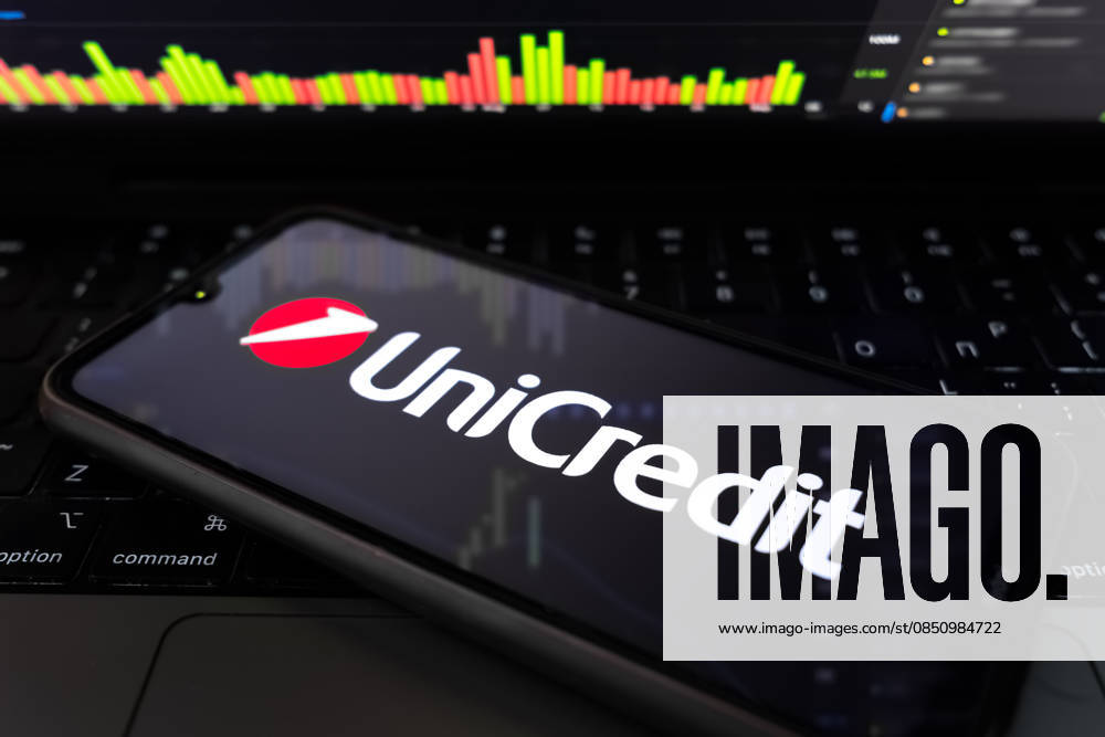UniCredit Sees Up To €500 Million In AI Cost Cuts In Next Years The UniCredit logo appears on a smartphone screen, and a stock exchange curve chart displays as the background on a laptop computer screen in this photo illustration in Athens, Greece, on March 18, 2026. UniCredit SpA Chief Executive Officer Andrea Orcel states the bank is quantifying the impact of artificial intelligence at about EUR400 million to EUR500 million ($576 million) in net cost reductions over roughly five years, driven by efficiency gains across core processes such as lending, compliance, and client onboarding. Athens Greece