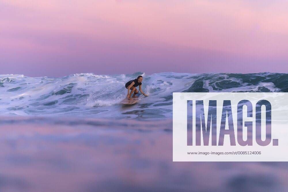 Distant view of single young woman surfing in sea at sunset, Kuta Lombok Indonesia TRKO020221 model released Symbolfoto