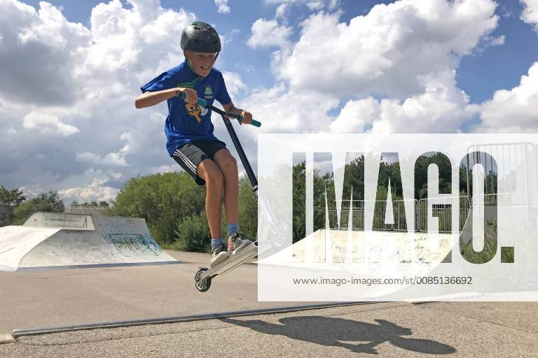 Young child 11 years old is riding on a stunt scooter in a skatepark skating rink