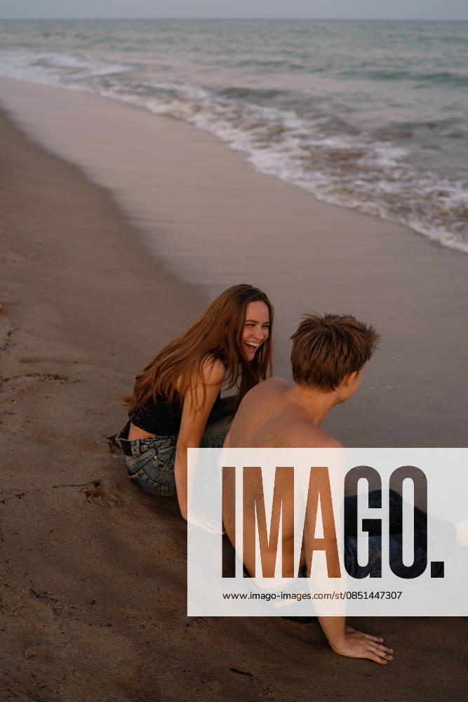 Young couple sitting side by side on sand at beach Castelldefels, Catalonia, Spain CR_NMDM260312-1980646-01 ,model released, Symbolfoto