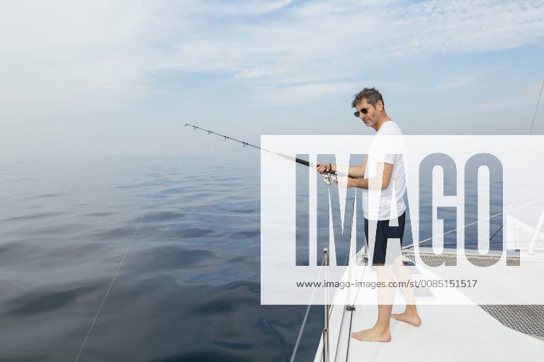 Mature man standing on catamaran, fishing model released Symbolfoto property released EBSF02576
