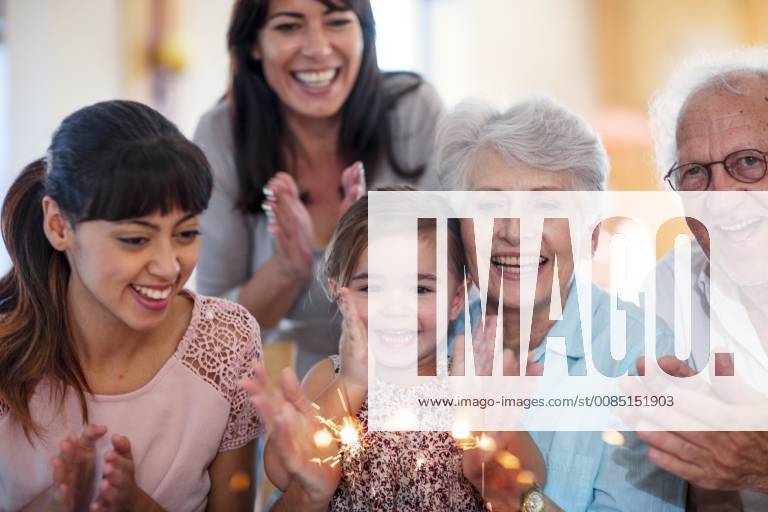 Little girl lwatching sparklers on a birthday cake, sitting on grandmother s lap, with family around model released Symbolfoto property released ZEF14253