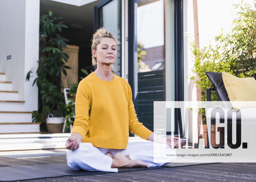 Woman meditating outdoors on sunny home terrace in yellow sweater model released, Symbolfoto property released, UUF36563