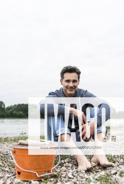 Portrait of smiling man with beer bottle and grill sitting at the riverside model released Symbolfoto UUF14509