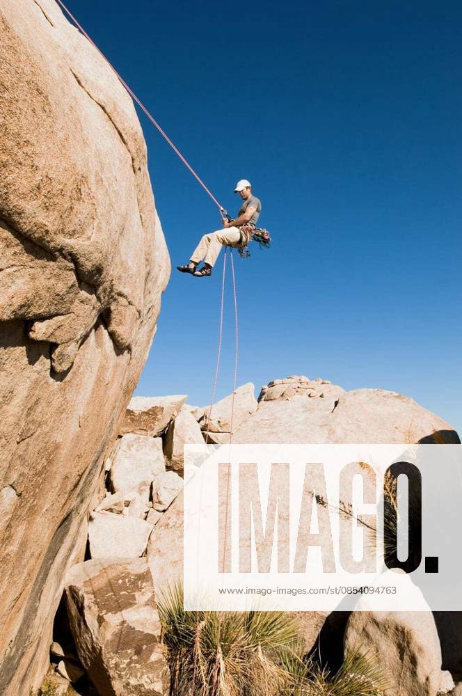 Man Rappelling From Cliff - Low angle view of a young man rappelling from cliff against clear blue sky model released Symbolfoto
