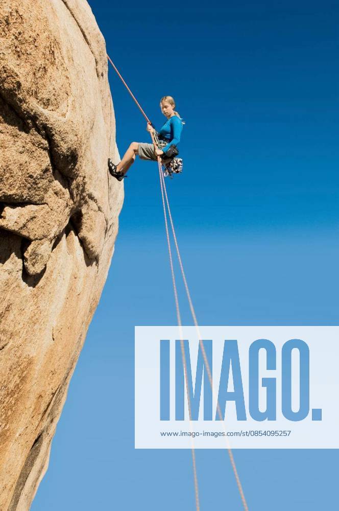 Woman Rappelling From Cliff - Low angle view of a young woman rappelling from cliff against clear blue sky model released Symbolfoto