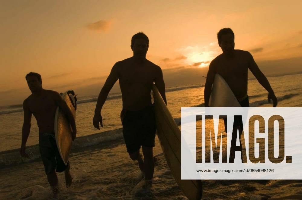 Surfers Carrying Surfboards Out Of Surf At Sunset - Full length of three surfers carrying surfboards out of surf at sunset model released Symbolfoto
