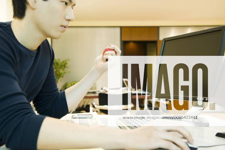 Office worker using computer, squeezing stress ball with one hand