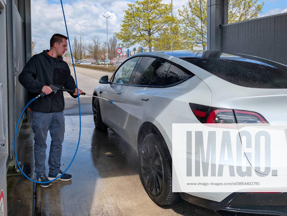 A man is cleaning his Tesla Model Y electric car at a self-service car wash using a pressure washer