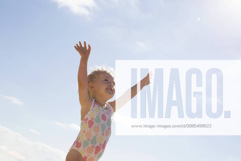 Little girl standing on beach with arms raised
