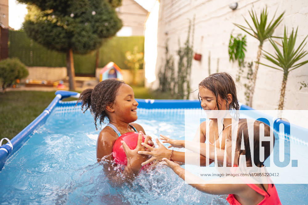 Drei Kinder, die in einem Swimmingpool im Garten mit einem Ball spielen Drei Kinder, die in einem Swimmingpool im Garten mit einem Ball spielen (License=RF) ,model released, Symbolfoto
