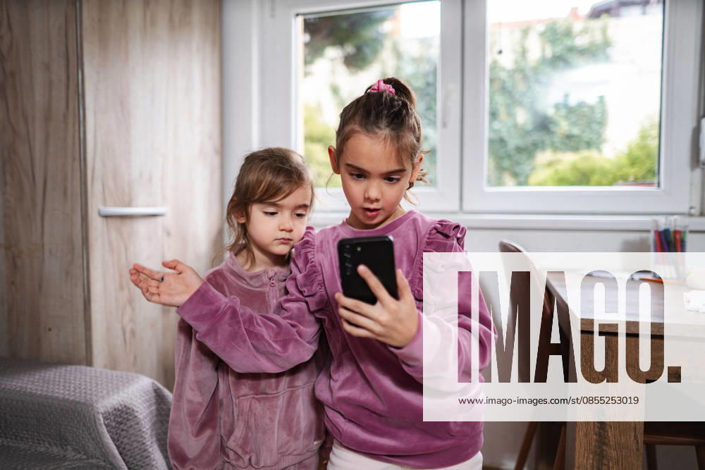 Zwei kleine Schwestern schauen sich gemeinsam in einem Kinderzimmer ein Smartphone an Little sisters sharing smartphone playing mobile game at home (License=RF) ,model released, Symbolfoto