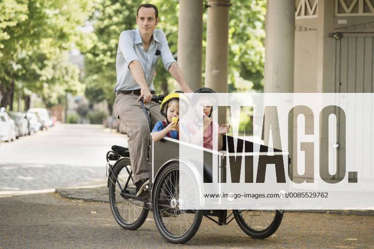 Father with boys riding bicycle with cart on street