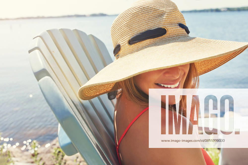 Put on your hats and take out the sunscreen. a cheerful young woman wearing a hat while being seated on a chair next to a lake outside in the sun (License=RF) ,model released, Symbolfoto