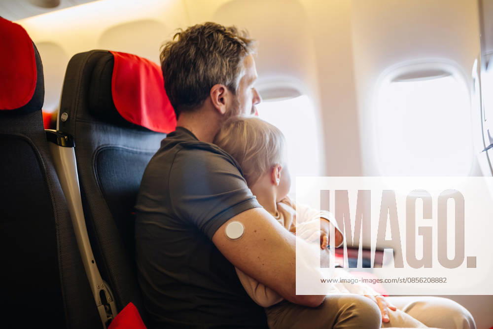 Diabetic father takign care of toddler during family flight. Diabetic father takign care of toddler during family flight. Traveling on airplane. model released