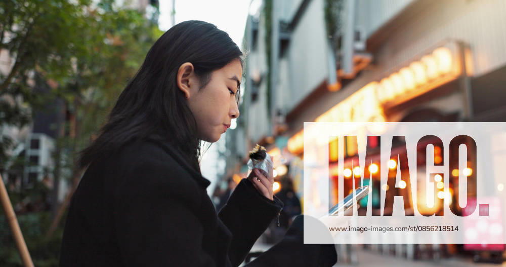 IMAGO Creative, Food, Japan, Onigiri Phone, eating and Asian woman with onigiri in the city on exploring vacation, adventure or holiday. Hungry, food and young female person enjoying a Japanese snack or meal in town on weekend trip (License=RF) ,model released, Symbolfoto