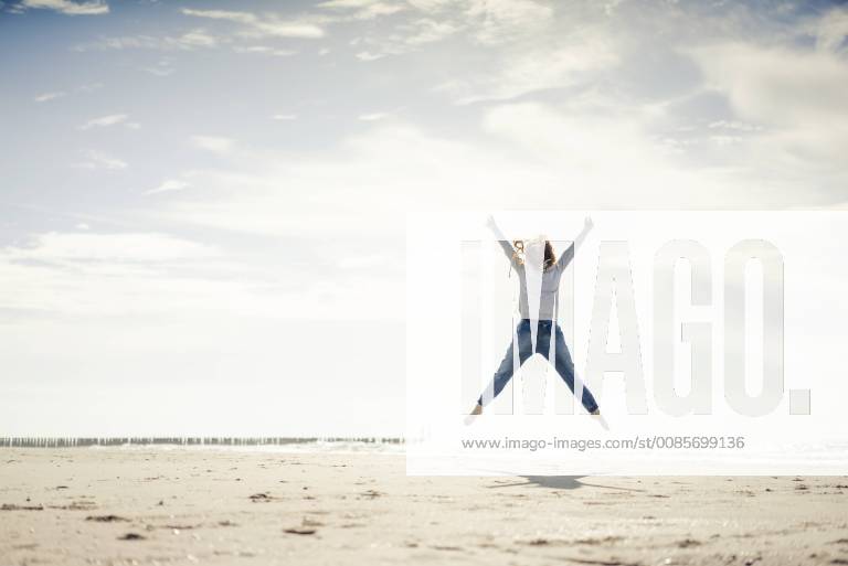 Happy woman having fun at the beach, jumping in the air model released Symbolfoto KNSF04325