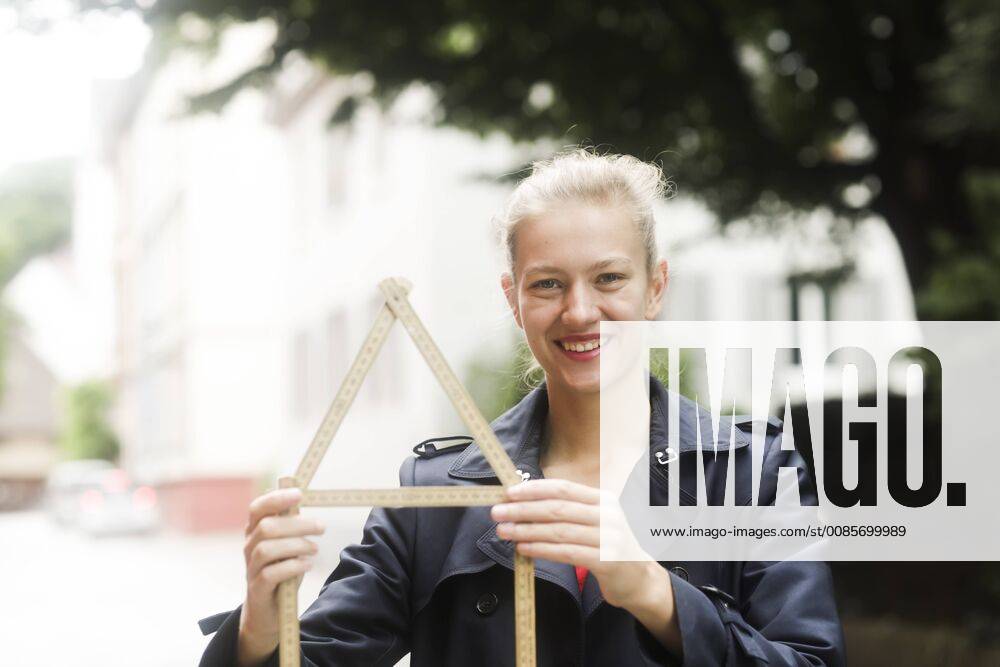 Portrait of smiling young woman holding pocket rule shaped like a house model released Symbolfoto SGF02196