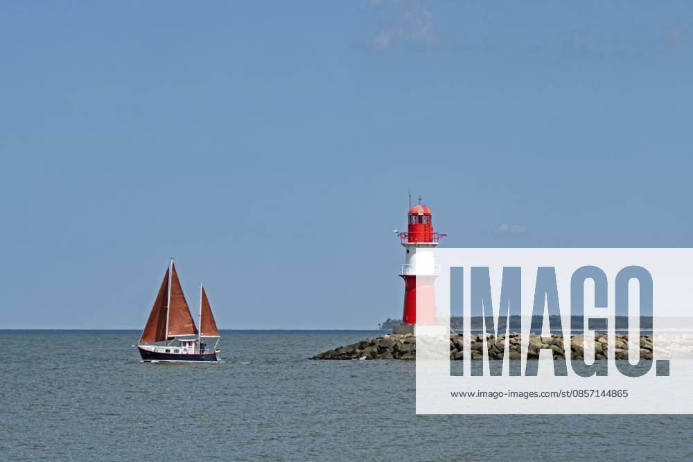 Ein Segelboot kreuzt in der Ostsee vor dem Leuchtturm von Rostock Warnemünde, Deutschland Ein Segelboot kreuzt in der Ostsee vor dem Leuchtturm von Rostock Warnemünde, Deutschland