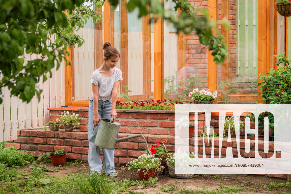Ein junges Mädchen gießt Pflanzen im Garten. A young girl is watering plants in a garden. She is wearing a white shirt and blue jeans (License=RF) ,model released, Symbolfoto