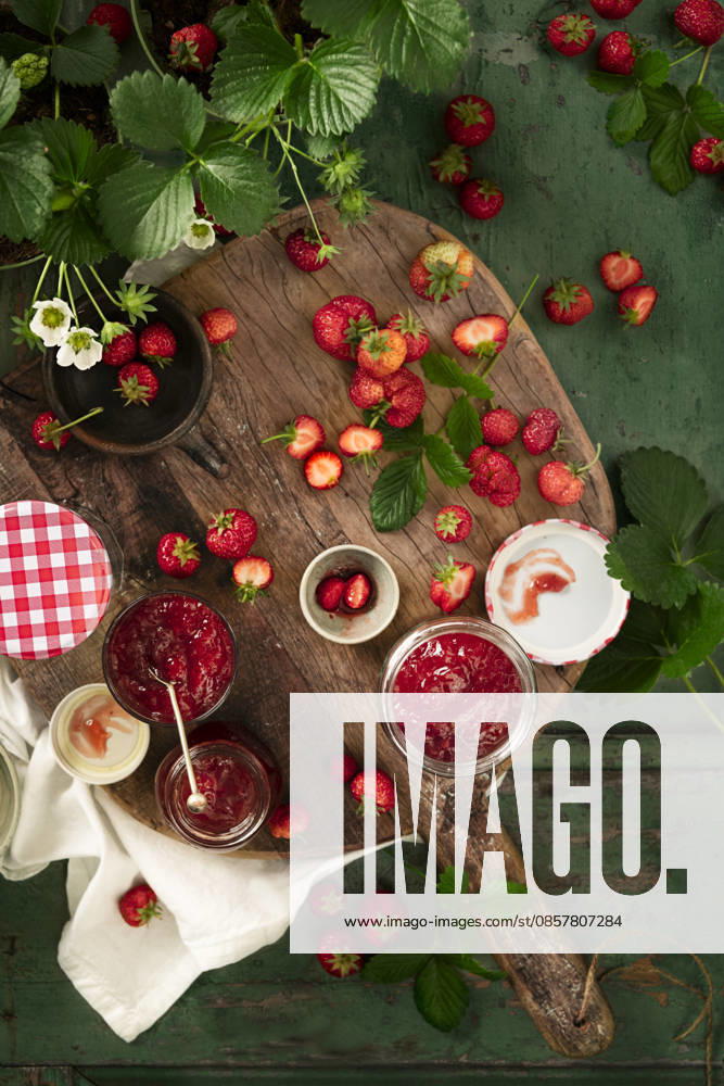 Flat lay of home made fresh strawberries jam in glass containers on wooden table and strawberry plants Flat lay of home made fresh strawberries jam in glass containers on wooden table and strawberry plants