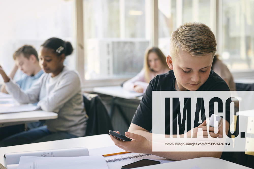 Junior high school student checking blood sugar level through glucose meter while sitting at desk with books in classroo Sweden, Stockholm, model released, property released