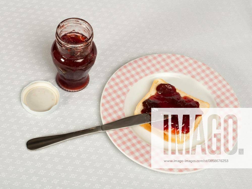 Spread jam on bread with knife and jar of jam. Pink checkered plate