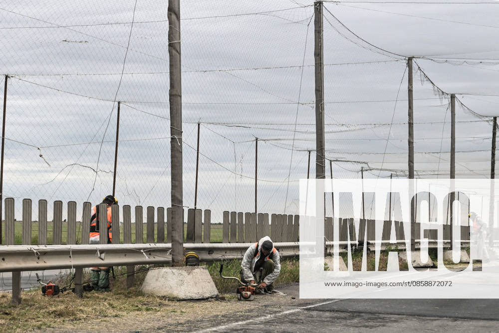 Municipal workers mow grass along the roadside of the Mykolaiv–Kherson highway, above which anti-drone netting has been installed to protect against Russian FPV drones, Kherson region, Ukraine, on June 3, 2026. The Russian army attacks the city daily with FPV drones and other unmanned aerial vehicles, deliberately terrorizing civilians. Russian forces conduct hunts for local residents, tracking them with FPV drones and dropping explosives. Police officers, medics, public transport, and urban infrastructure are also targeted (Photo by Dmytro Smolienko Ukrinform) Life under shelling in frontline Kherson