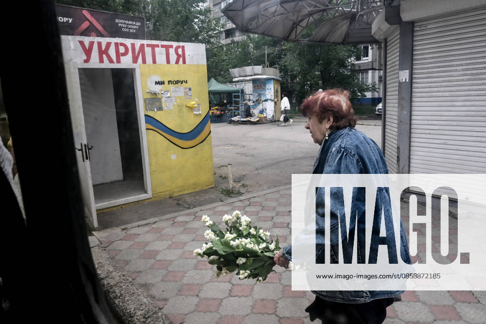 A woman carrying a bouquet of mock-orange blossoms walks past a mobile concrete shelter in the frontline city of Kherson, Ukraine, on June 2, 2026. The Russian army attacks the city daily with FPV drones and other unmanned aerial vehicles, deliberately terrorizing civilians. Russian forces conduct hunts for local residents, tracking them with FPV drones and dropping explosives. Police officers, medics, public transport, and urban infrastructure are also targeted. Based on the intensity of attacks, Kherson is informally divided into yellow and red zones, with the red zone considered the most dangerous due to constant shelling and drone strikes. Anti-drone netting has been installed above roads to help protect against Russian FPV dron