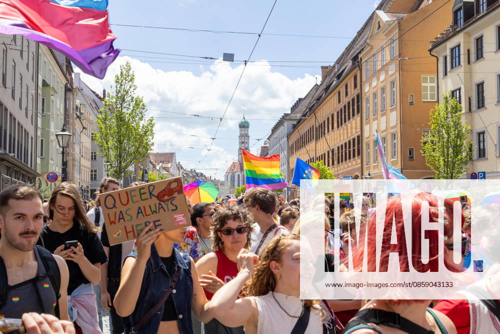 Augsburg, Bavaria, Germany June 13, 2026: Participants carrying rainbow flags and wearing colorful costumes take part in Christopher Street Day (CSD) in Augsburg. The parade through the city center promotes the rights of LGBTQ+ people as well as social diversity and tolerance. A participant holds a sign reading: QUEER WAS ALWAYS HERE