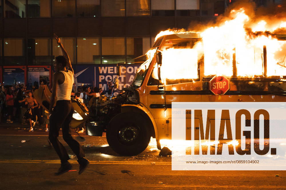 A man with a white shirt on jumps in the air with his hand raised as he runs past a yellow school bus that was lit ablaze during the celebration of the New York Knicks winning the NBA Finals. New York USA - ZUMAf193 20260614_znp_f193_002