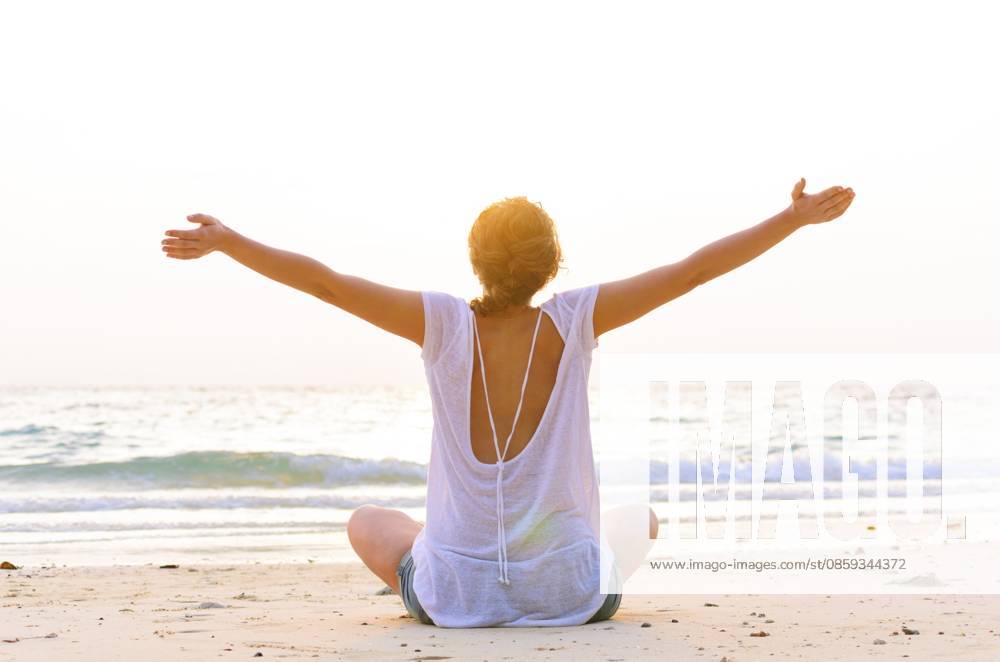 Junge Frau sitzt bei Sonnenaufgang am Strand Young woman is sitting on beach at sunrise