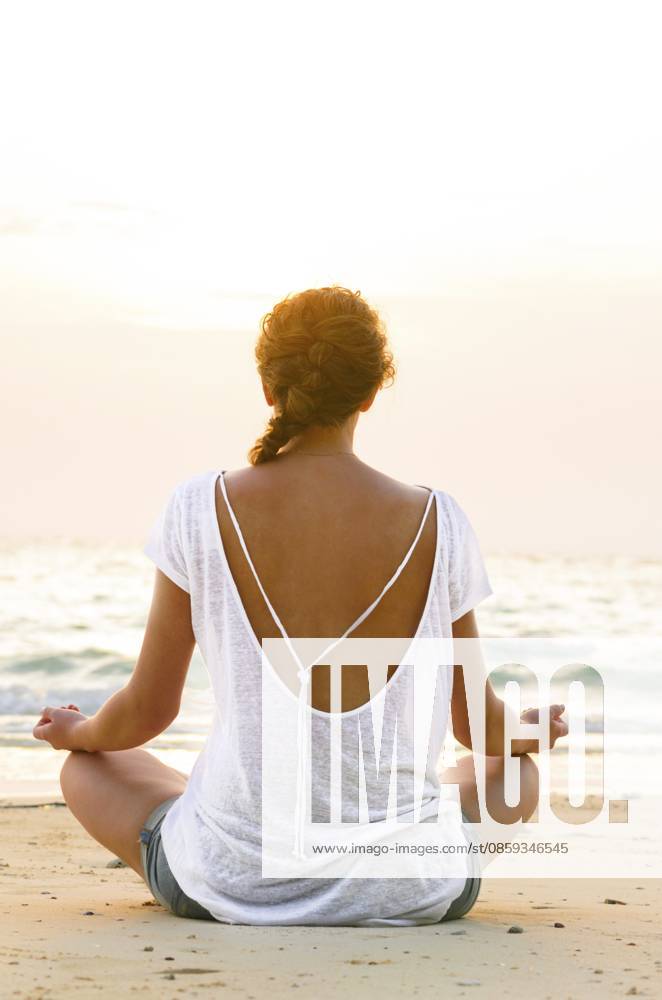 Junge Frau sitzt bei Sonnenaufgang am Strand Young woman is sitting on beach at sunrise