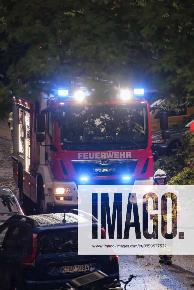 A Cologne fire department truck with flashing blue lights during a continuous emergency operation in Cologne-Nippes; firefighters clearing fallen trees and blocked roads after a severe storm with heavy thunderstorms and gales. Nordrhein-Westfalen Deutschland, Germany DSCF6991