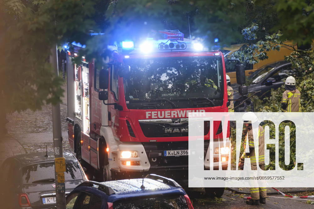 A Cologne fire department truck with flashing blue lights during a continuous emergency operation in Cologne-Nippes; firefighters clearing fallen trees and blocked roads after a severe storm with heavy thunderstorms and gales. Nordrhein-Westfalen Deutschland, Germany DSCF6995