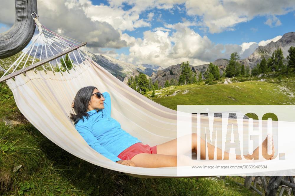 Wanderin ruht sich in einer Hängematte auf einer Berghütte auf dem Tre Cime Weg in den Dolomiten aus und genießt die alpine Landschaft, ein Wellness Abenteuer und eine Wanderpause Female hiker resting in hammock at mountain hut on Tre Cime trail in Dolomites enjoying alpine scenery wellness adventure and hiking break