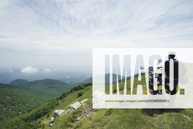 Man standing by motorcycle on top of mountain, rear view