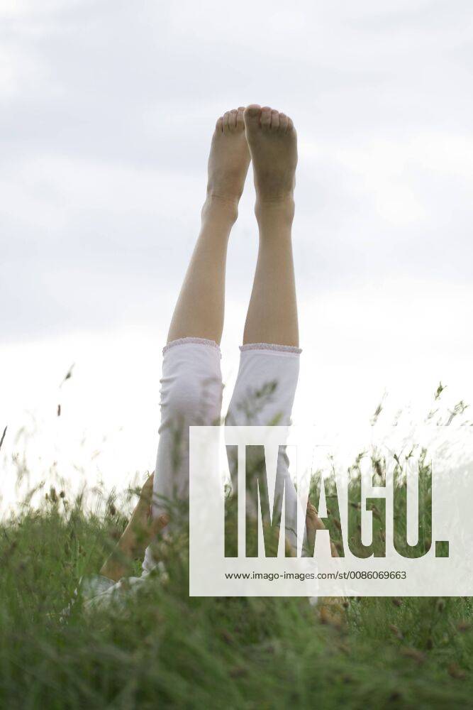 Girl lyingon back in tall grass with legs raised in the air