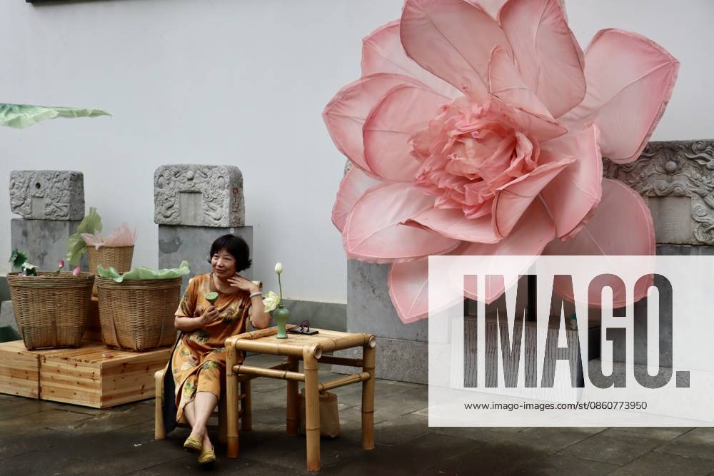 A visitor poses for photo in front of a giant lotus art installation during a lotus market at the Confucius Temple on July 4, 2026 in Hangzhou, Zhejiang Province of China.