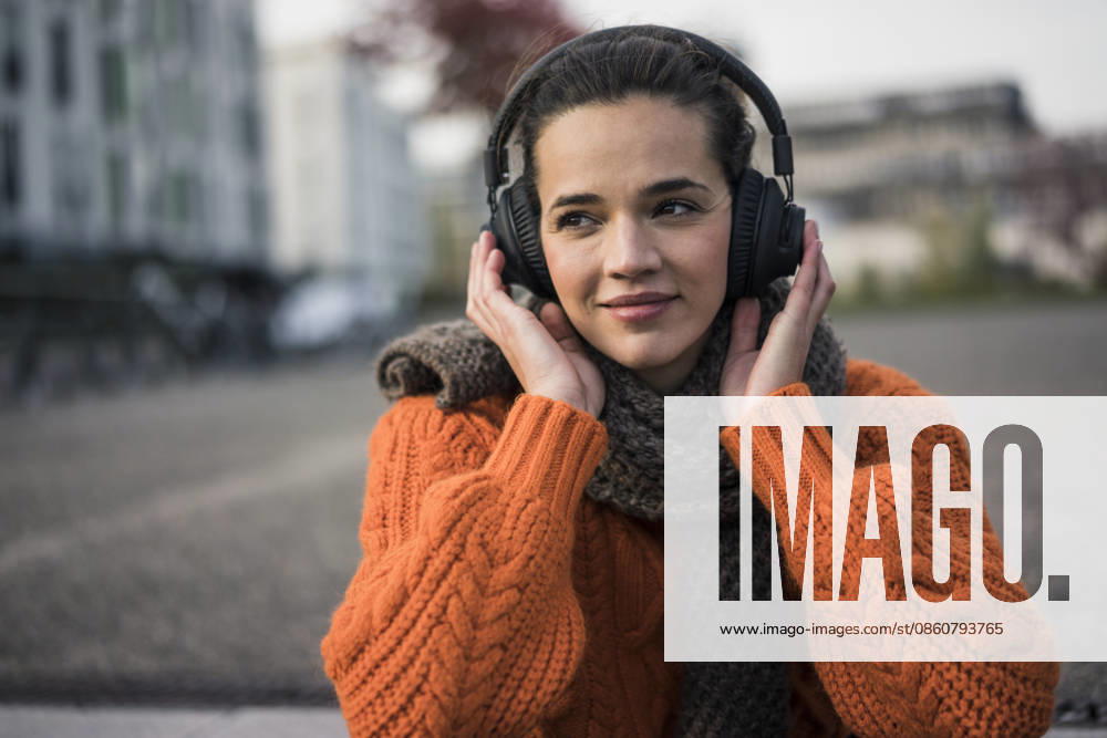 Portrait of woman wearing scarf and orange knit pullover outdoors listening music with cordless headphones model released, Symbolfoto, MOEF01878