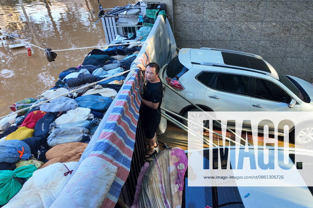 Residents stand guard near a makeshift flood barrier constructed from sandbags and vehicles to protect parked cars at the Shengshi Jiayuan residential complex on July 10, 2026 in Guigang, Guangxi Zhuang Autonomous Region of China. The local authorities beef up restoration efforts after torrential rains caused by Typhoon Maysak.