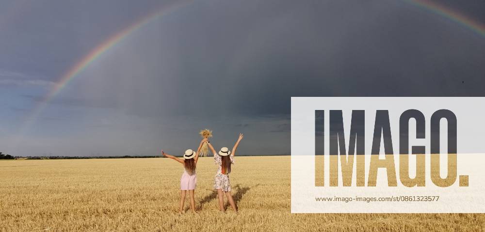 In einem Weizenfeld nach dem Regen laufen zwei Mädchen. Bunte echte Regenbogen über den Horizont. europe Ukraine. Sommerpflanzenfelder, reifendes Weizenfeld. In a wheat field after the rain, two girls run. Colorful real rainbow over the horizon. europe Ukraine. Summer crop fields, ripening wheat field. High quality photo (License=RF) ,model released, Symbolfoto