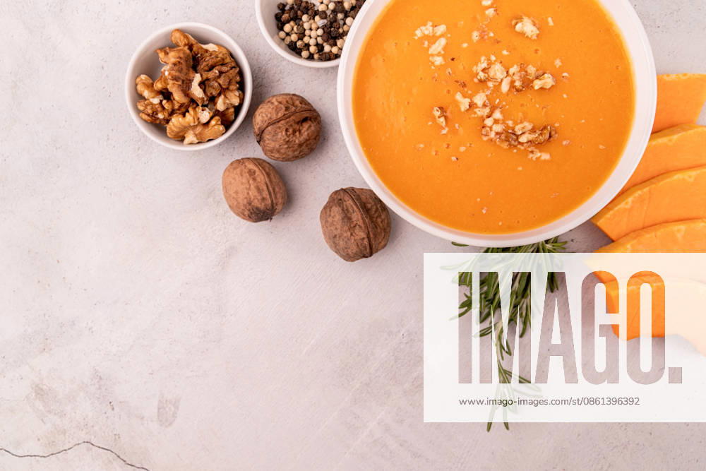 Kürbissuppe mit Walnüssen in einer weißen Schüssel, garniert mit Kürbisscheiben und Gewürzen ? Draufsicht auf weißem Marmorhintergrund mit Freiraum für Text Pumpkin soup with walnuts in white bowl decorated with pumpkin slices and spices top view flat lay with copy space (License=RF)