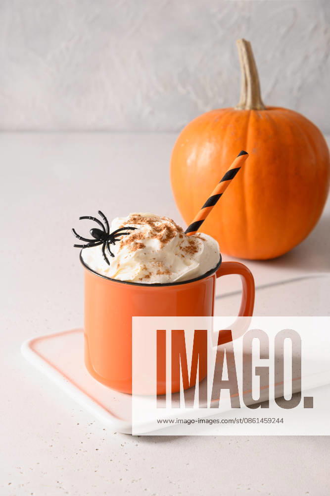Halloween-Kürbis-Latte mit Schlagsahne und Spinnen als Garnitur Pumpkin latte coffee with whipped cream decorated spiders in orange mug on white kitchen background. Vertical format. Funny food for child in Halloween party. (License=RF)