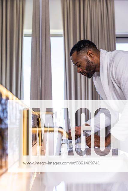 Senior African American man in bathrobe washing hands at bathroom sink with gold faucet, copy space, model released, property released, 27.01.2026 06:00:00, 10615960