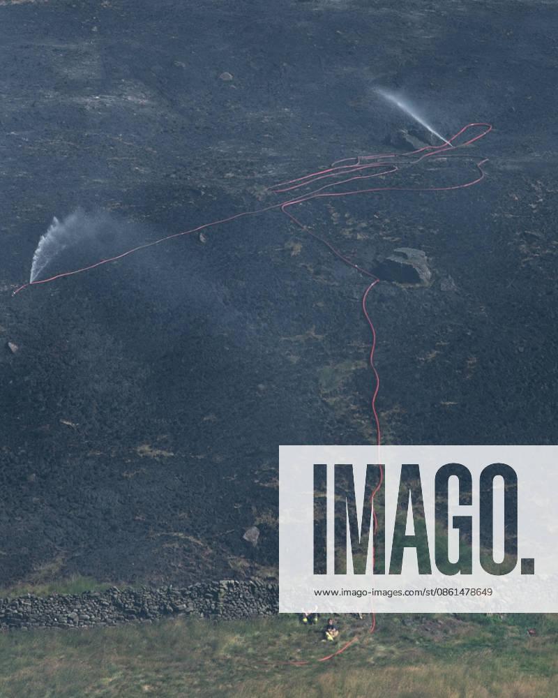 Firemen sit by water hose attempting to put out smouldering moorland close to Dove Stone Reservoir in Greater Manchester on 13 July 2026. Greater Manchester Police have arrested a woman in connection with a large moorland fire at Dove Stone Reservoir in Greenfield. The blaze, burning since Saturday, is under active investigation, with officers following leads regarding reports of fireworks nearby. The 20-year-old suspect remains in custody as the cause of the fire is yet to be officially determined. Oldham Greater Manchester England Dovestone Reservoir