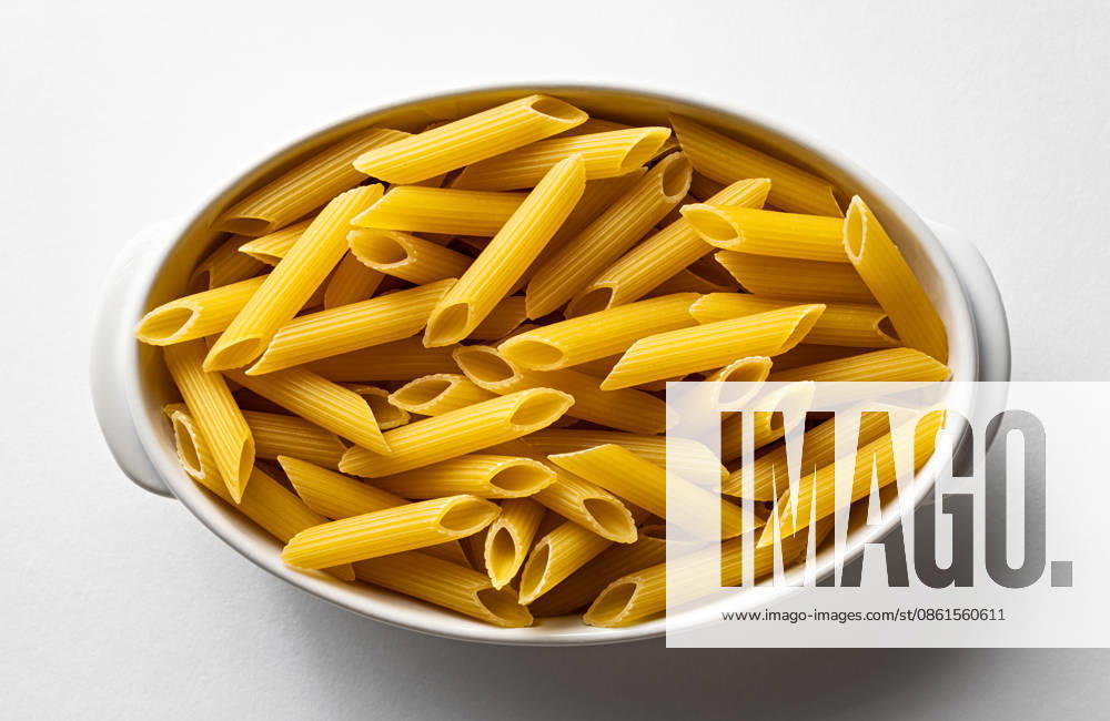 Nahaufnahme von ungekochten Penne-Nudeln in einer ovalen Schüssel als einfaches, isoliertes Lebensmittel-Stillleben Close top view of uncooked penne pasta in an oval dish as a simple isolated food still life (License=RF)