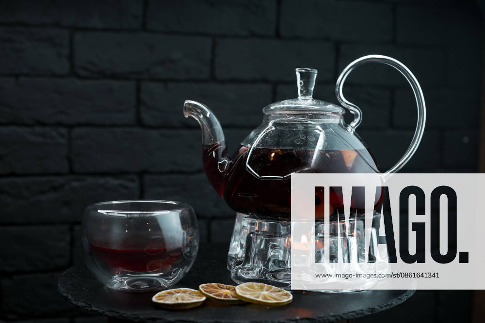 Schwarzer Aromatic Herbal tea with Minzblättern and Ginger and Oranges and Fruit slices in a antique Glass teapot next to a Glass cup at a Wooden table in a cafà Beautiful Tea service a Tea 1102838702